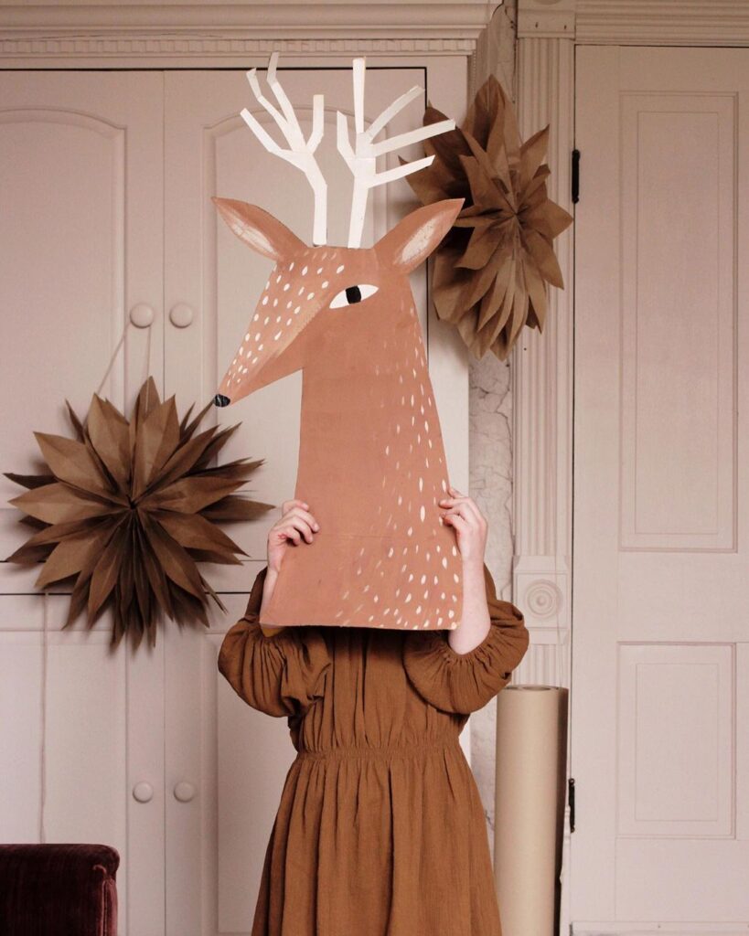 Tête de renne réalisée en papier, tenue par un enfant.